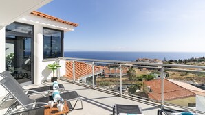Un balcon avec vue sur la mer, aménagé avec des fauteuils et une table, et une porte vitrée donnant sur un espace intérieur.