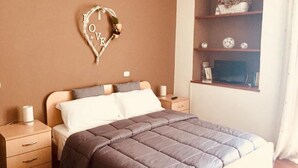 Ein Schlafzimmer mit Bett, Nachttischen, Ablagefläche und einer Regal mit Dekorationsobjekten, sowie einer herzförmigen Dekoration an der Wand.