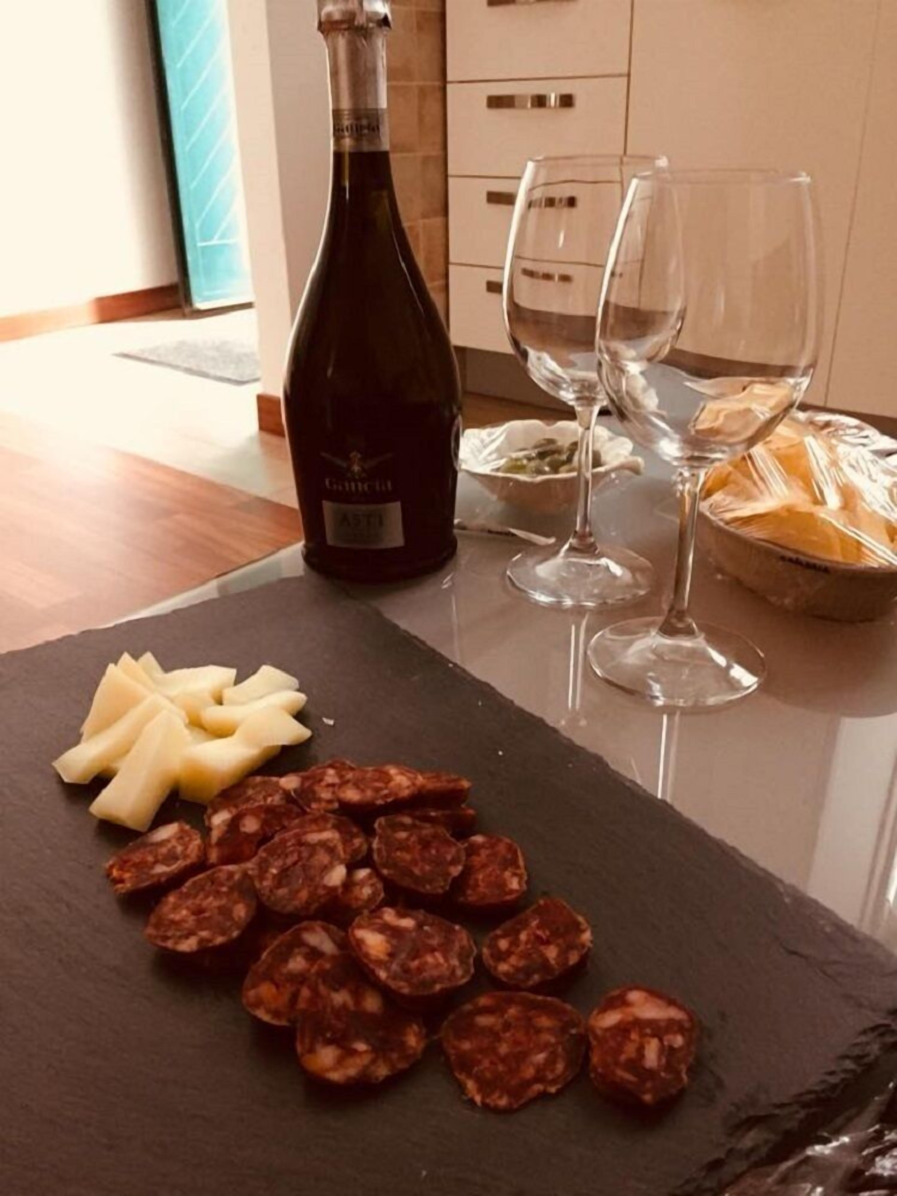 A kitchen counter with a bottle of wine, two glasses, sliced cheese, and cured meats.