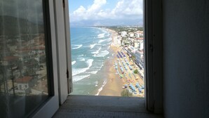 Blick aus einem Fenster auf einen Strand mit Sonnenschirmen und Gebäuden.