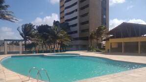 A swimming pool with a curved design, surrounded by a tiled patio. - Apartamento Luxo vista mar, muito aconchegante VP803 (Fortaleza)