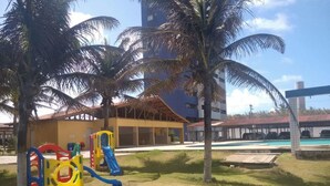 A playground with slides and climbing structures, a swimming pool, and a building with a red roof. - Apartamento Luxo vista mar, muito aconchegante VP803 (Fortaleza)