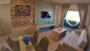 A living room with a brick wall, a flat-screen TV, a sofa, a coffee table, and a dining area with chairs. - Apartamento Luxo vista mar, muito aconchegante VP803 (Fortaleza)