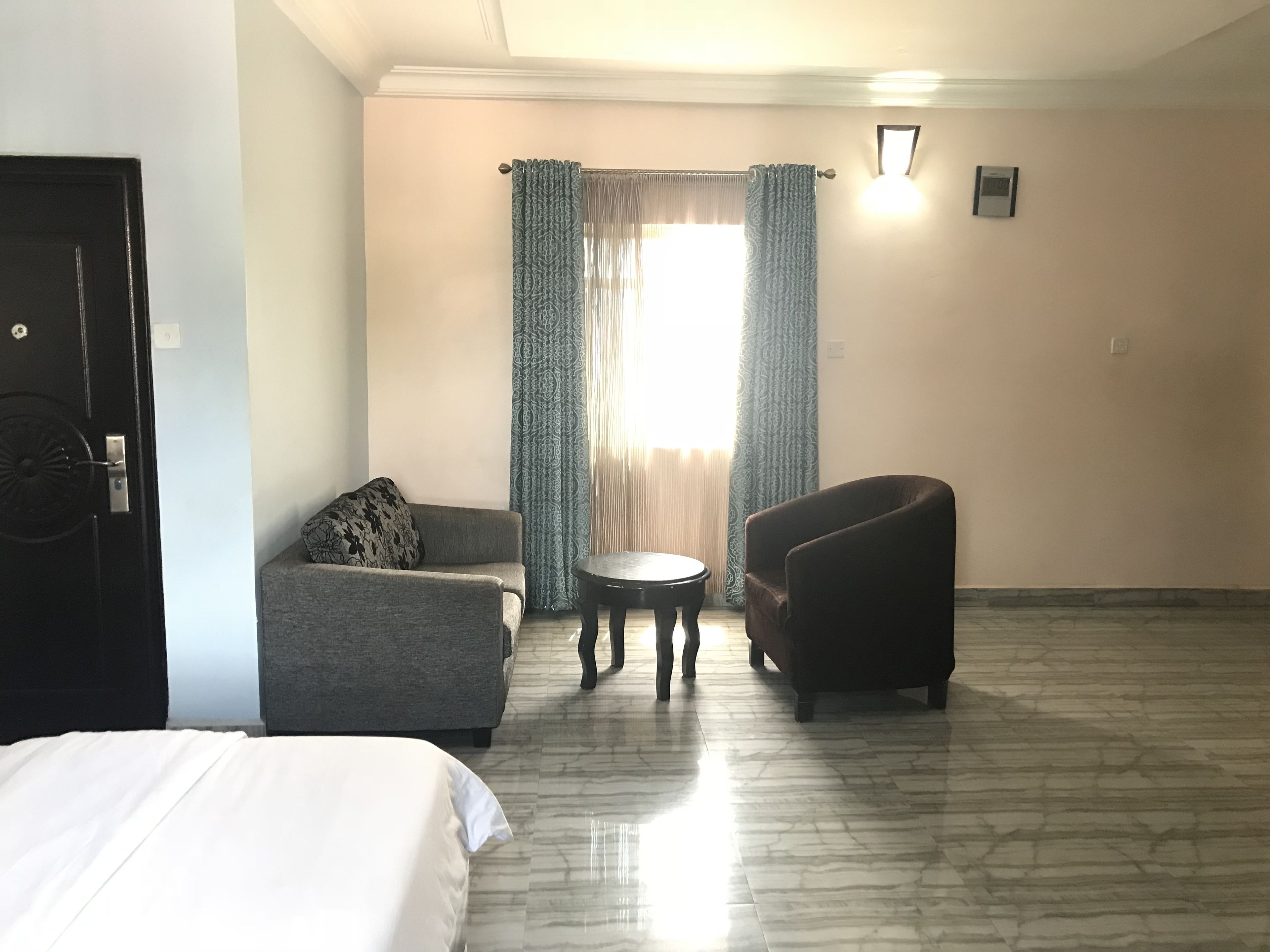 A hotel room with a bed, two armchairs, a small round table, and a window with curtains.
