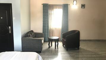 A hotel room with a bed, two armchairs, a small round table, and a window with curtains.