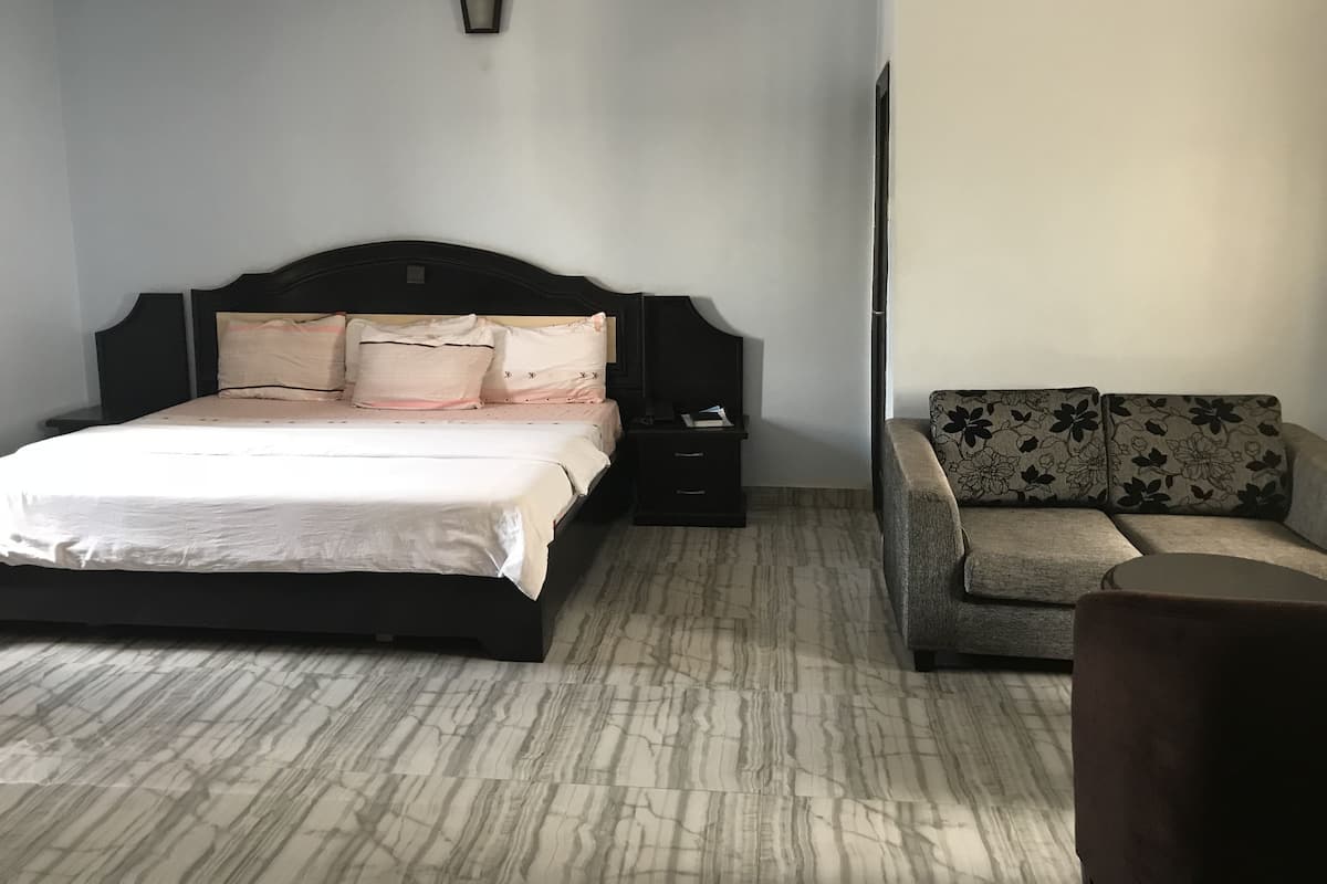 A bedroom with a bed, a nightstand, a sofa, and a wall-mounted light fixture.