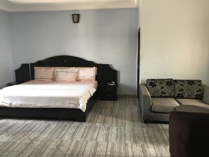 A bedroom with a bed, a nightstand, a sofa, and a wall-mounted light fixture. - PennyHill Suites and Resorts (Enugu)