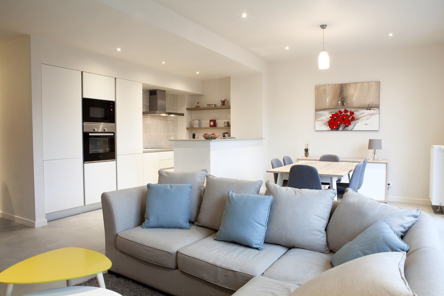 A modern living room with a sofa, a dining table, and a kitchen area with appliances.