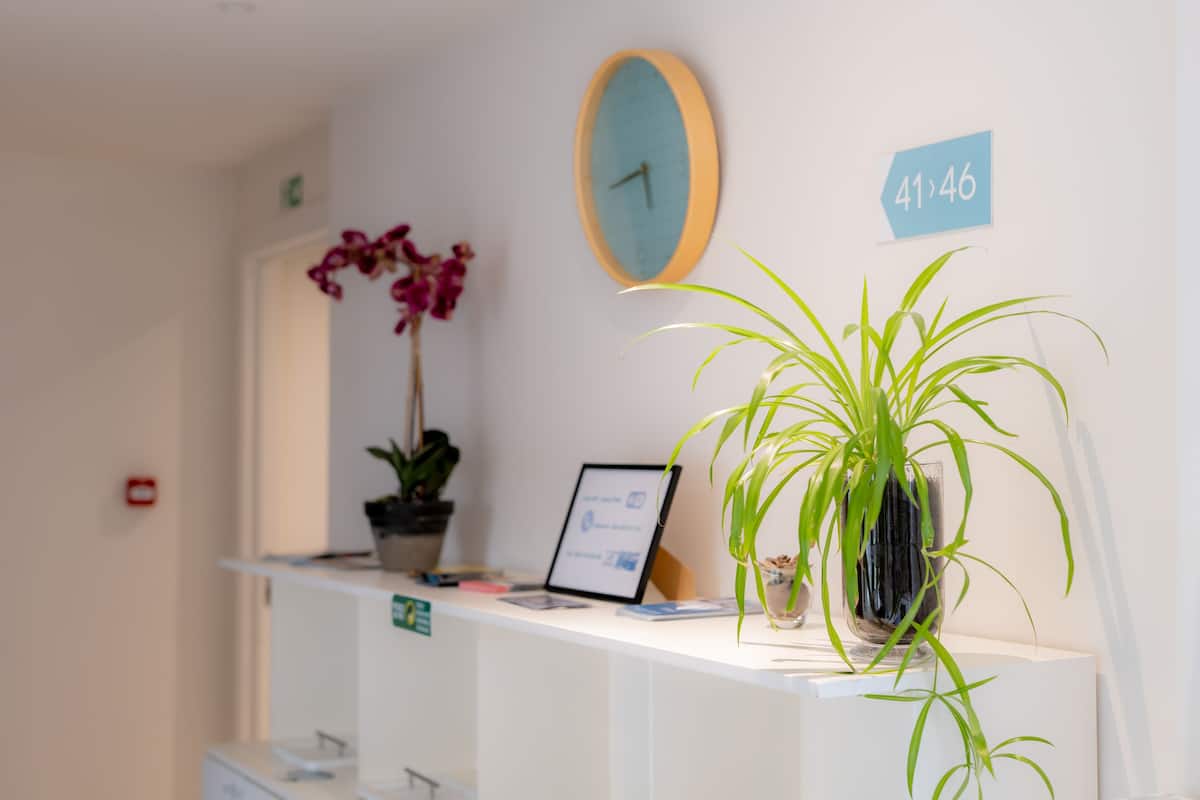 A reception desk with a clock, a sign indicating room numbers, and two potted plants.