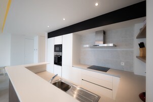 Una cocina moderna con un lavamanos de acero inoxidable, armarios blancos y encimera negra.