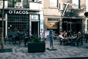 Un área de estar al aire libre con mesas y sillas, un letrero que dice 'O'TACOS' y un letrero de 'LOUNGE BAR' que dice 'ELVET'.