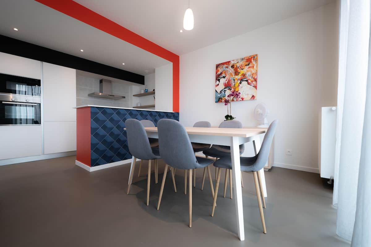 A modern kitchen with white cabinets, a red accent wall, and a dining area with a table and chairs.