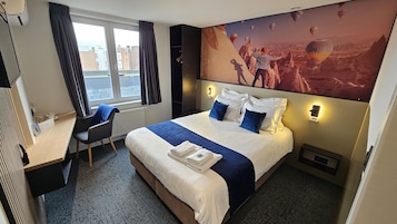 Habitación de hotel con una cama grande, un escritorio, una silla y vistas a la ciudad por la ventana.