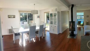Un espacio habitable amplio con una mesa de comedor y sillas, un mueble blanco, una chimenea y vistas al exterior.