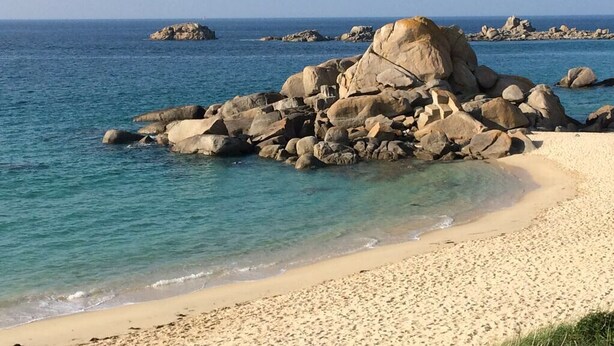 Una playa con rocas grandes y agua azul cristalina.