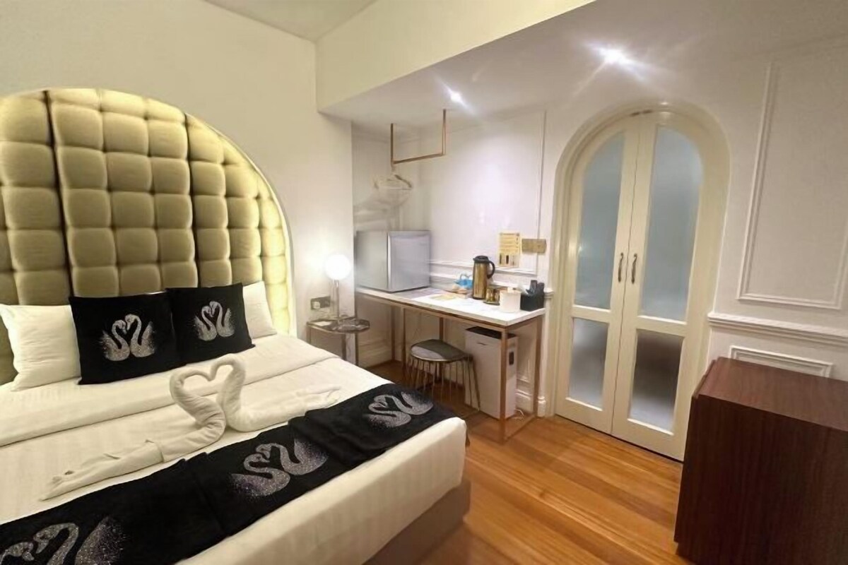 A hotel room with a large bed, a desk, a wardrobe, and a small kitchenette.