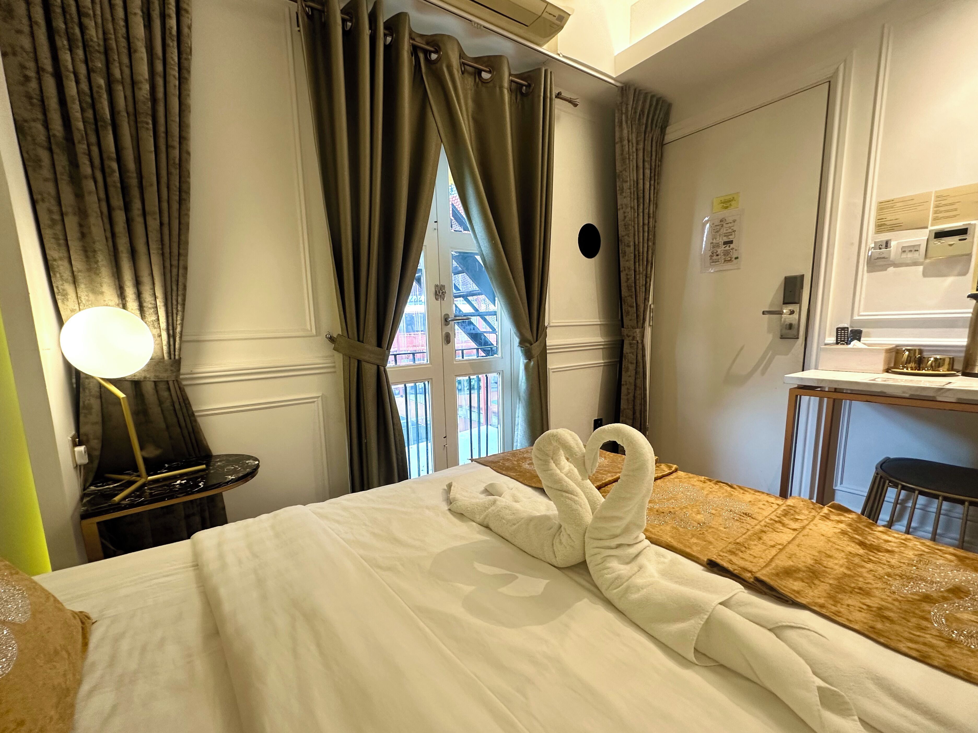 A hotel room with a bed, a desk, a chair, a lamp, and a window with curtains.