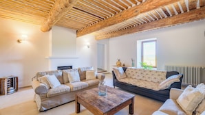 Een ruime woonkamer met een houten plafond, twee banken, een salontafel en een open haard.