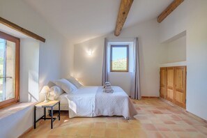 Une chambre à coucher avec un lit, une table de chevet avec une lampe, une fenêtre avec des rideaux et une armoire en bois.