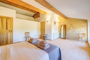 Une chambre à coucher avec un lit, deux chaises, un plafond en bois et un mur en pierre.