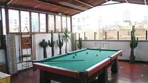 Un tavolo da biliardo in una stanza con ampie finestre, piante di cactus e un muro piastrellato.