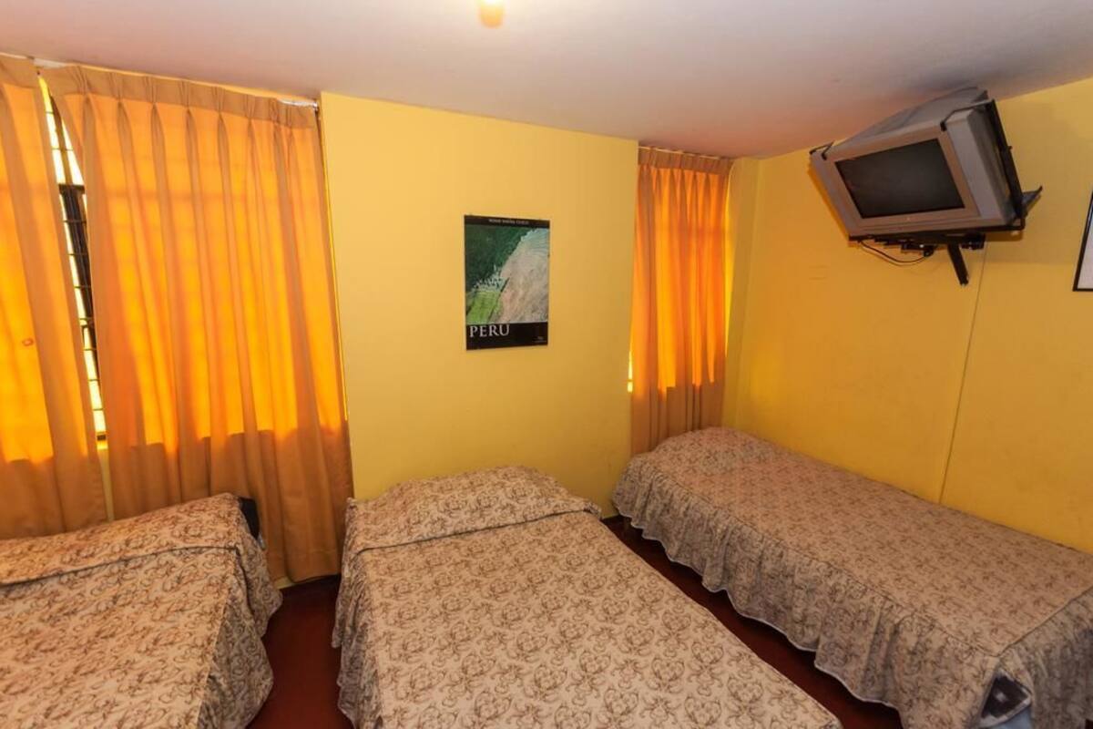 A room with two single beds, a poster of Peru on the wall, and a television mounted on the wall.