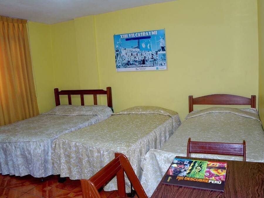 Una habitación con dos camas individuales, una silla de madera, una mesa con un libro y un cartel en la pared.
