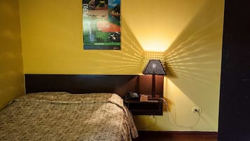 A hotel room with a bed, a nightstand, a lamp, and a poster on the wall.
