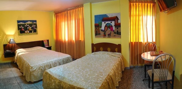 Une chambre d’hôtel avec deux lits, une petite table avec une chaise, une lampe et deux tableaux accrochés aux murs.