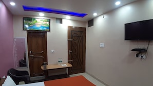 Quarto de hotel com cama, televisão na parede, escrivaninha com cadeira e porta com detalhes decorativos.