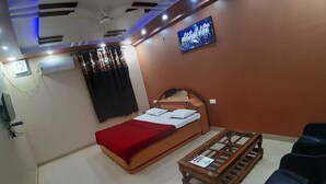 Quarto com cama, televisão na parede, mesa pequena e duas cadeiras.
