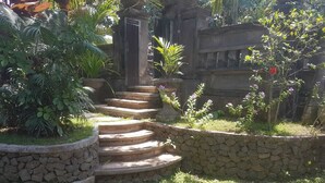 A stone staircase leading up to a door, surrounded by lush greenery and a stone wall. - A Newly 1-Bedroom House with Open Kitchen Overlooking to Garden (Amed)