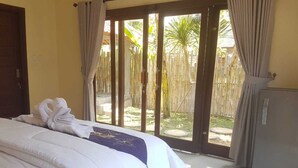 A hotel room with a bed, a wardrobe, and a sliding glass door leading to a garden. - A Newly 1-Bedroom House with Open Kitchen Overlooking to Garden (Amed)