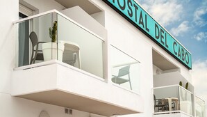 Een hotel met een balkon, een bordje met de tekst 'OSTAL DEL CABO' en een heldere lucht.
