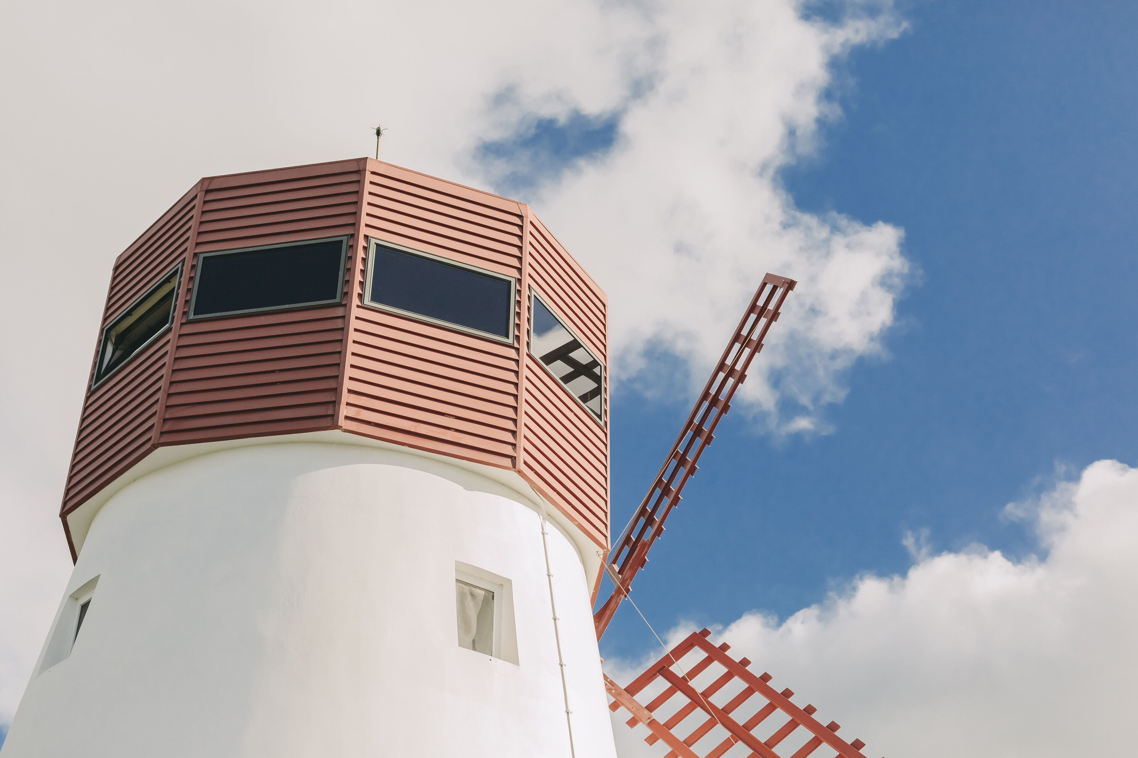 Un moulin à vent avec une base blanche et une structure supérieure marron, doté de deux fenêtres et d’une échelle.