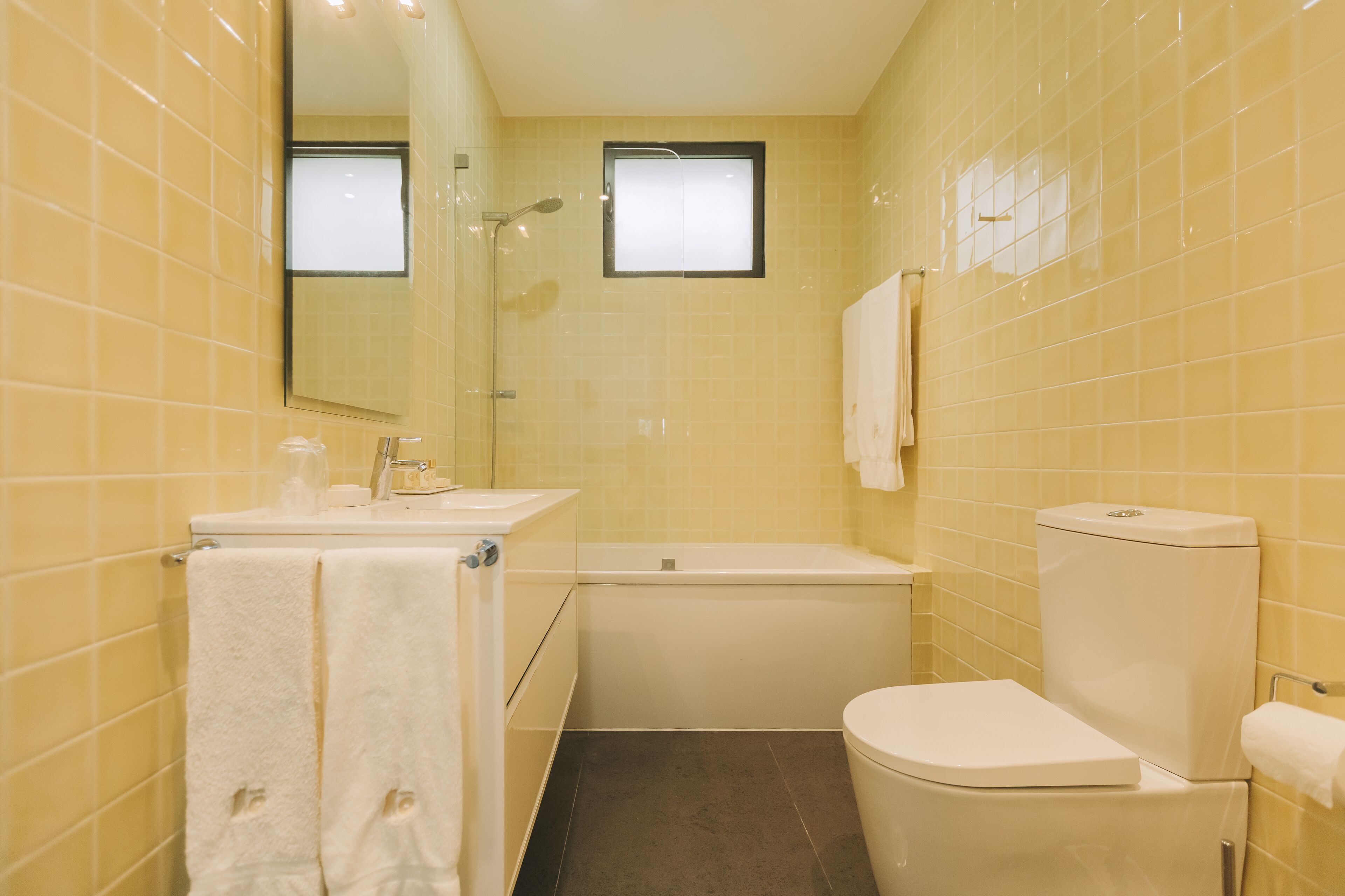 Une salle de bain avec des murs recouverts de carreaux jaunes, un lavabo blanc, une baignoire et des toilettes.
