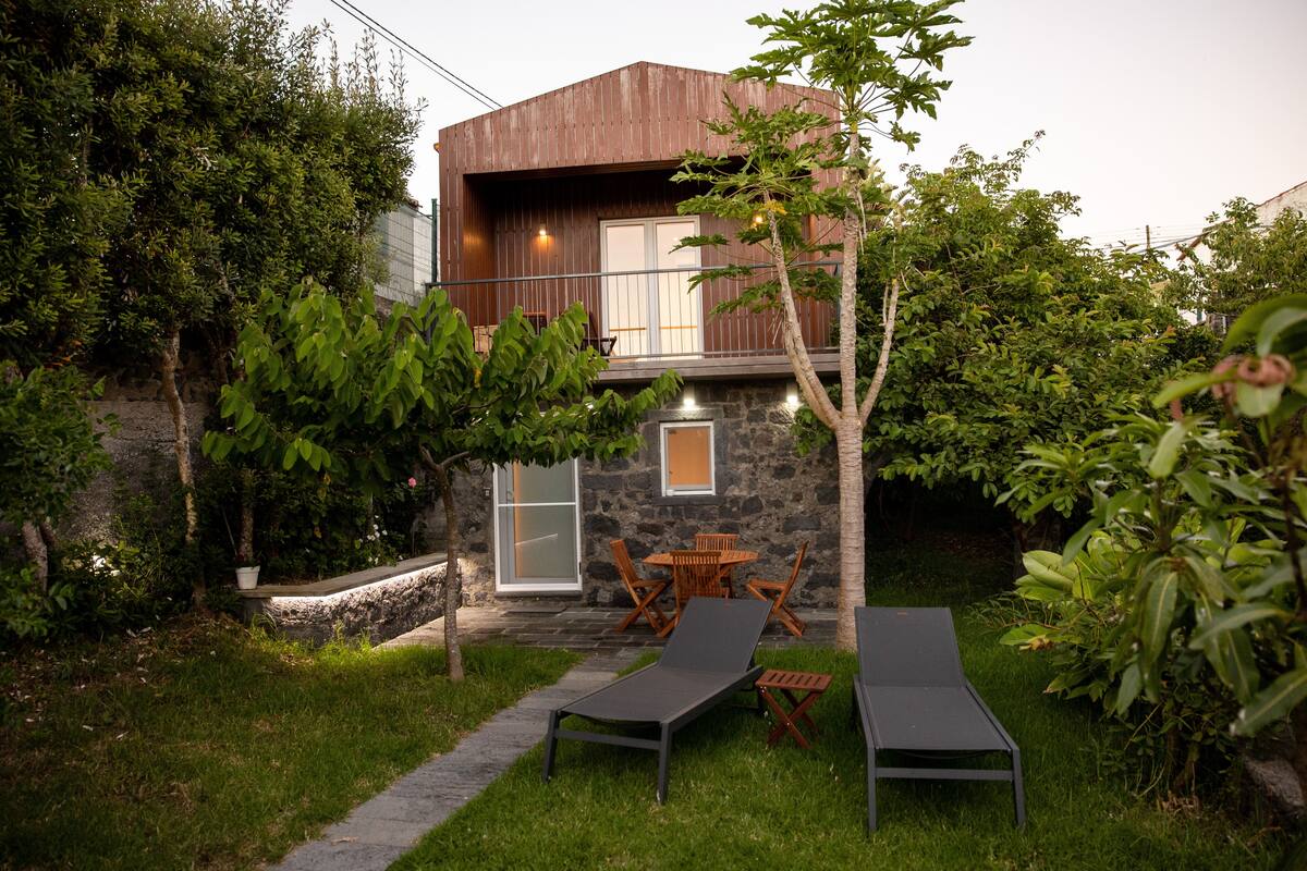 A modern house with a stone facade, a balcony, and a small patio area with outdoor furniture.