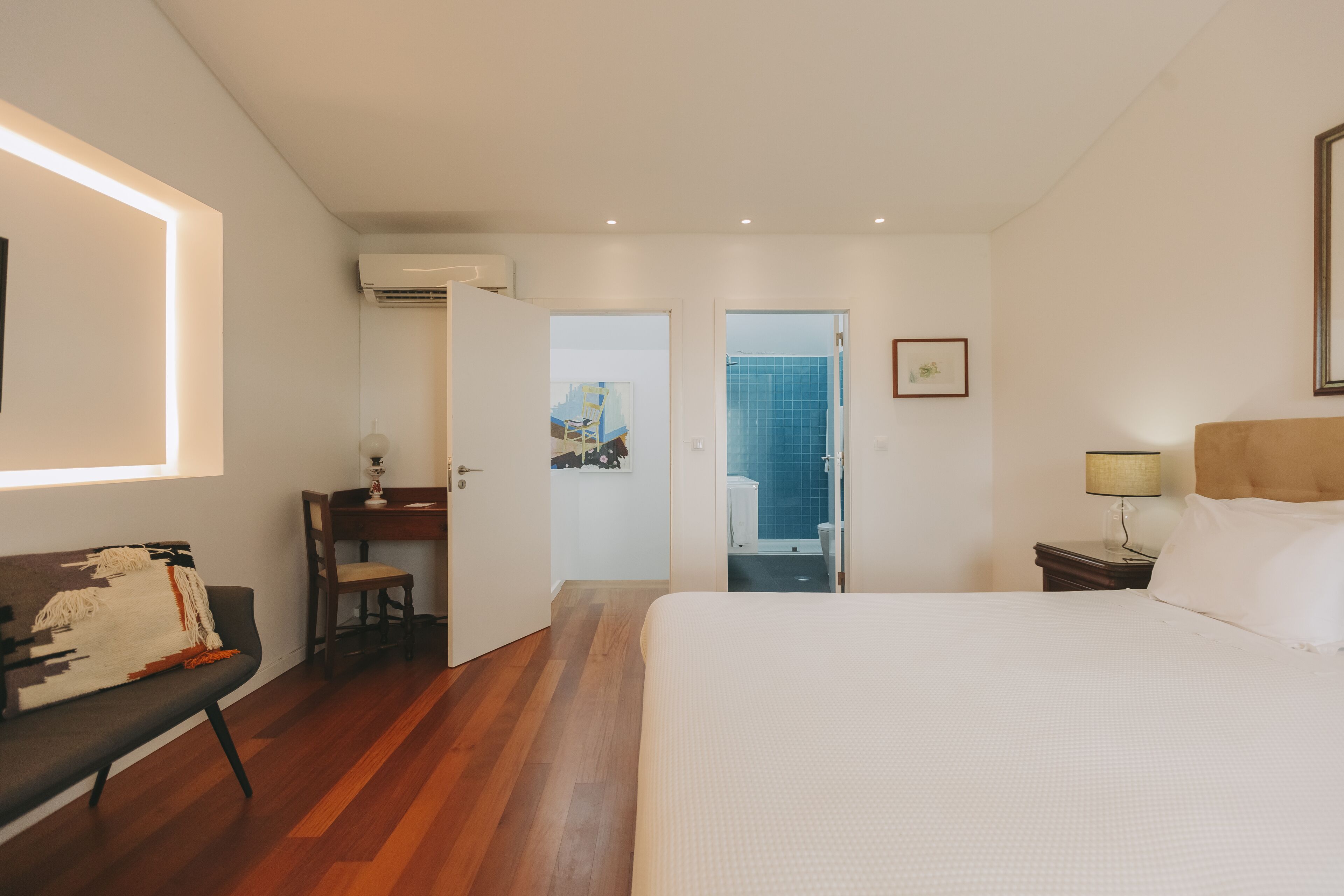 A hotel room with a bed, a desk, a chair, and an air conditioning unit.