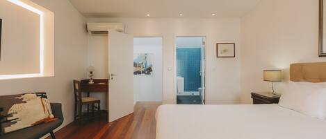 A hotel room with a bed, a desk, a chair, and an air conditioning unit.