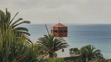 A lighthouse with a red roof, surrounded by greenery and overlooking the sea.