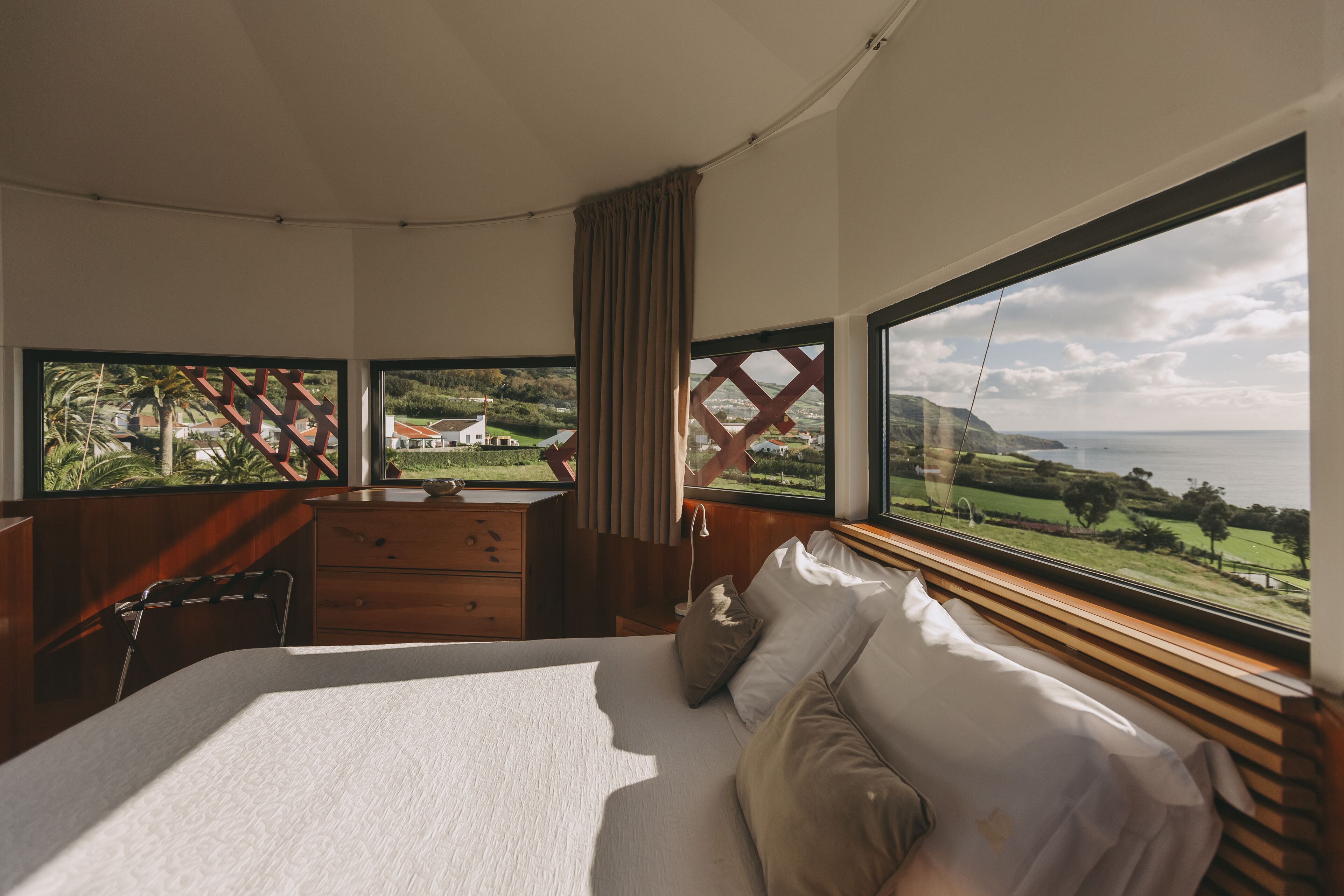 Un dormitorio con una cama grande, un escritorio y vistas al mar y a la vegetación.