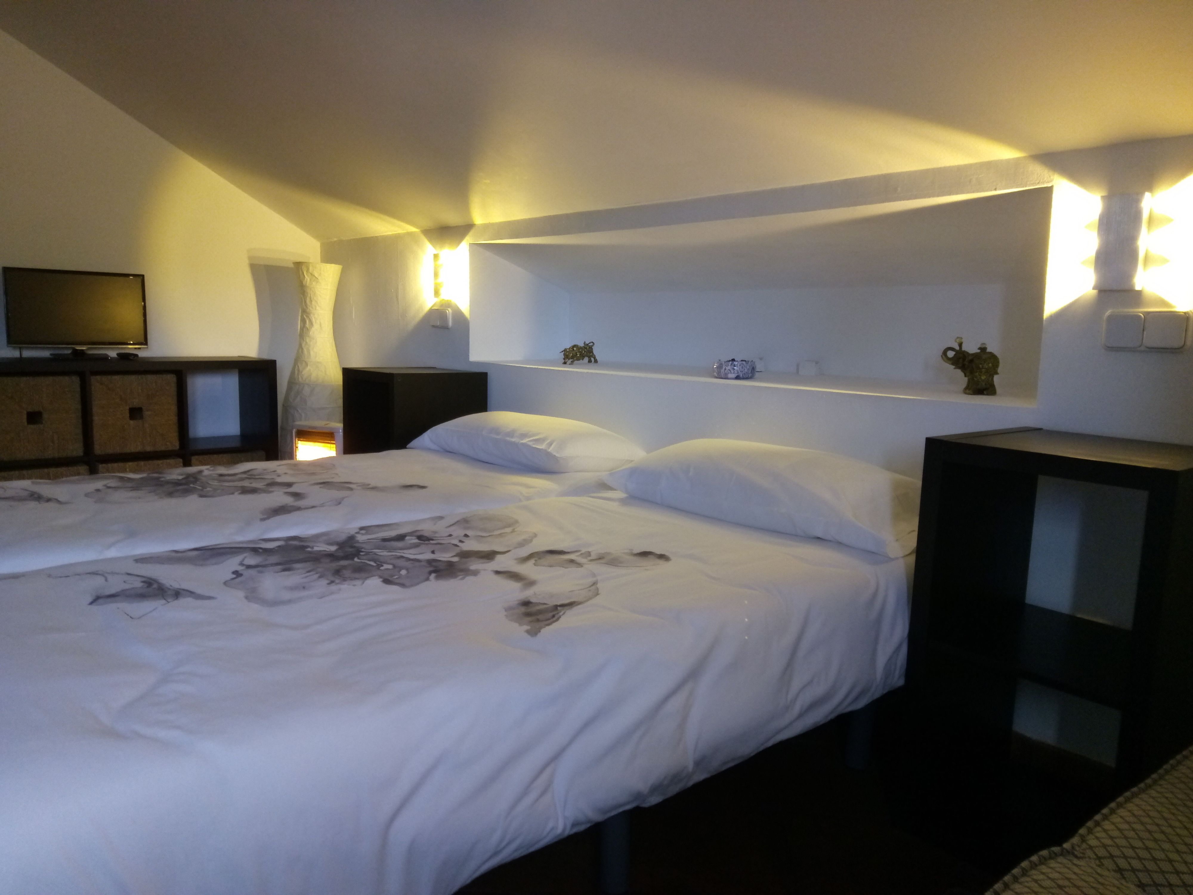 A bedroom with a large bed, a TV on a dresser, and wall-mounted lights.