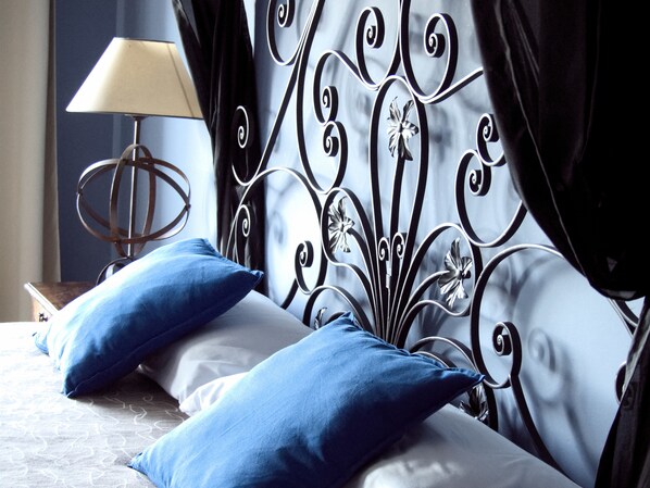 Una cama con almohadas azules y un cabecero metálico con motivos florales.