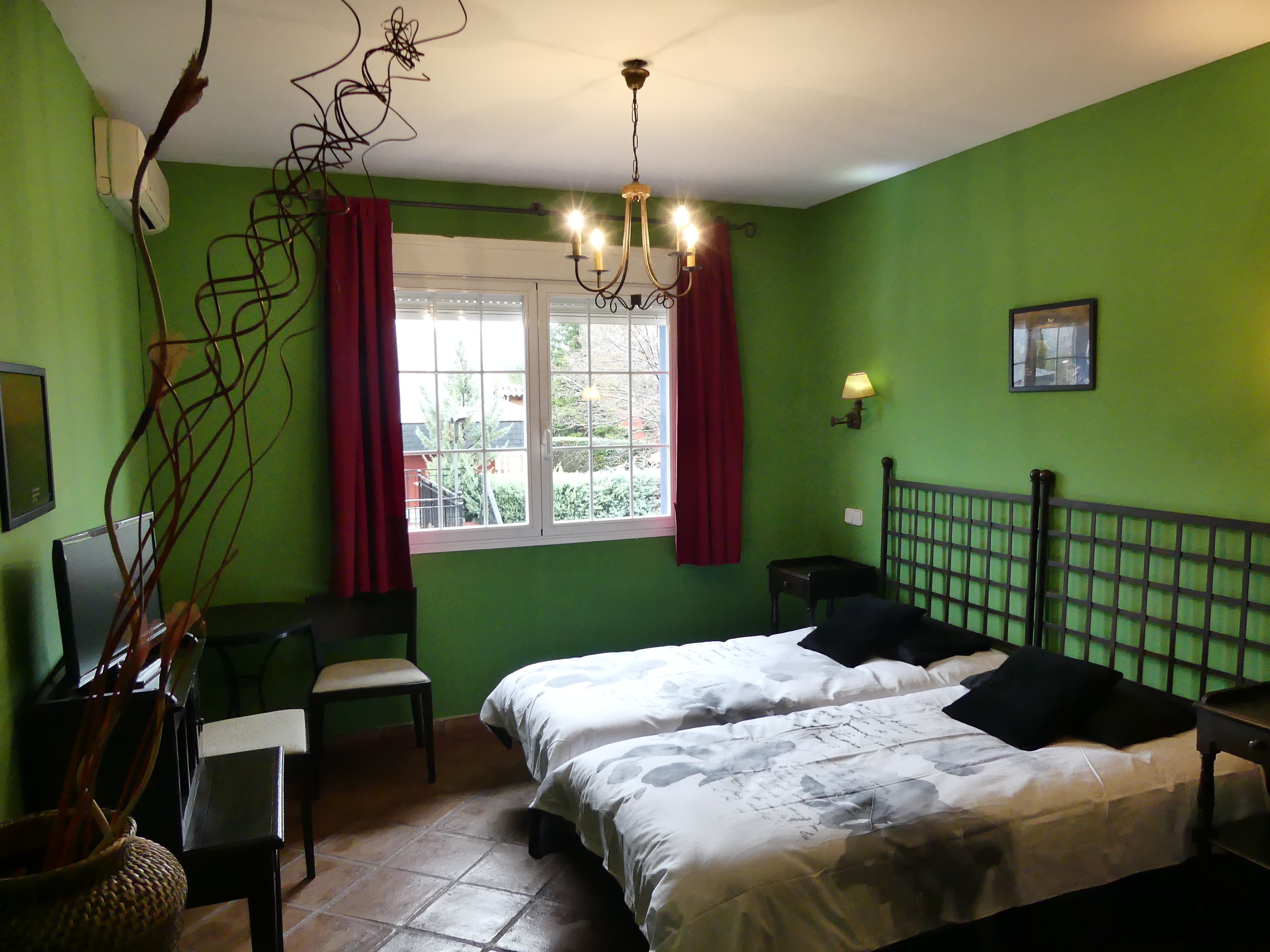 A room with two beds, a desk, a chair, a window with curtains, a lamp, and a picture on the wall.