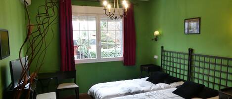 A room with two beds, a desk, a chair, a window with curtains, a lamp, and a picture on the wall.