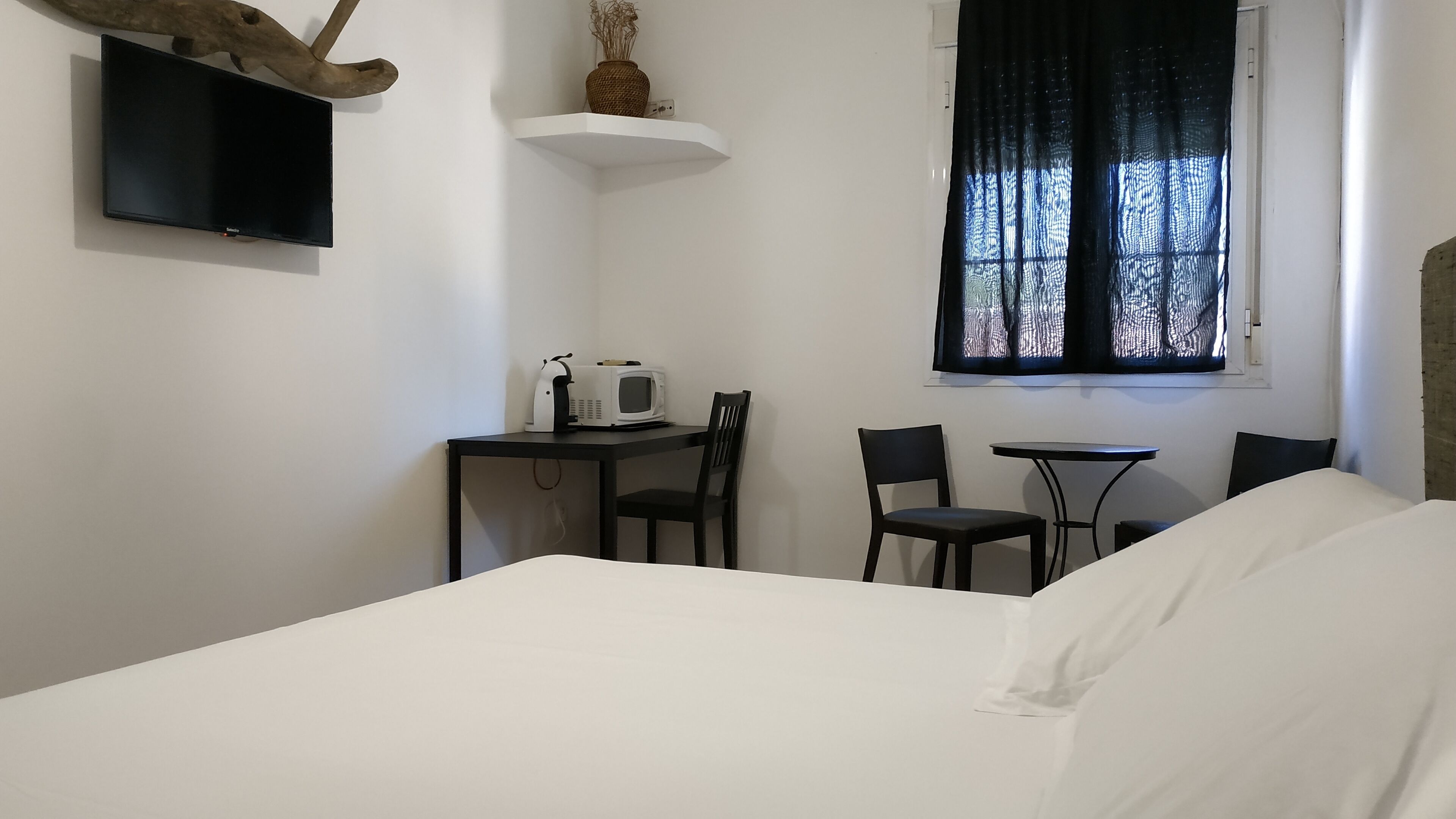 A bedroom with a bed, a desk with a chair, a microwave, and a TV mounted on the wall.