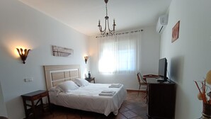 A hotel room with a bed, a desk with a computer, a chair, a TV, and a chandelier. - Alojamiento la Pedriza (Manzanares el Real)