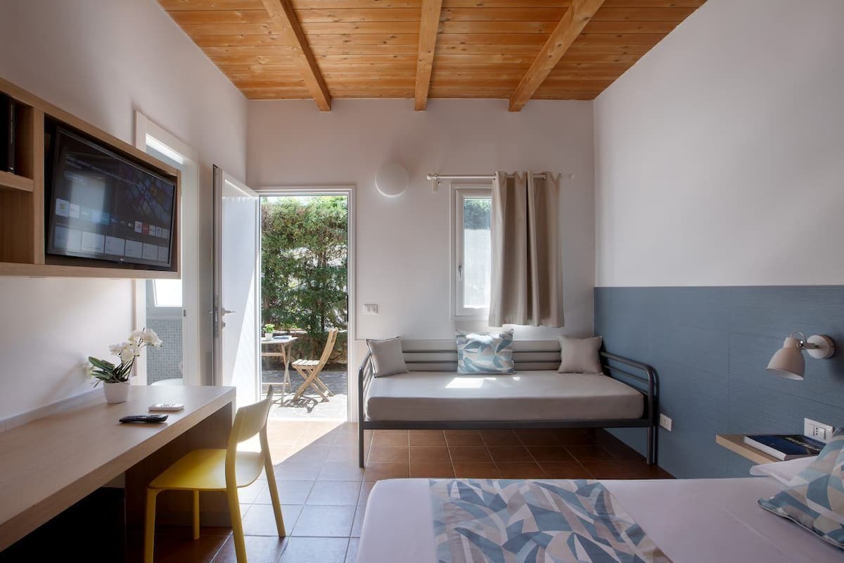A bedroom with a bed, a desk, a TV, and a window.