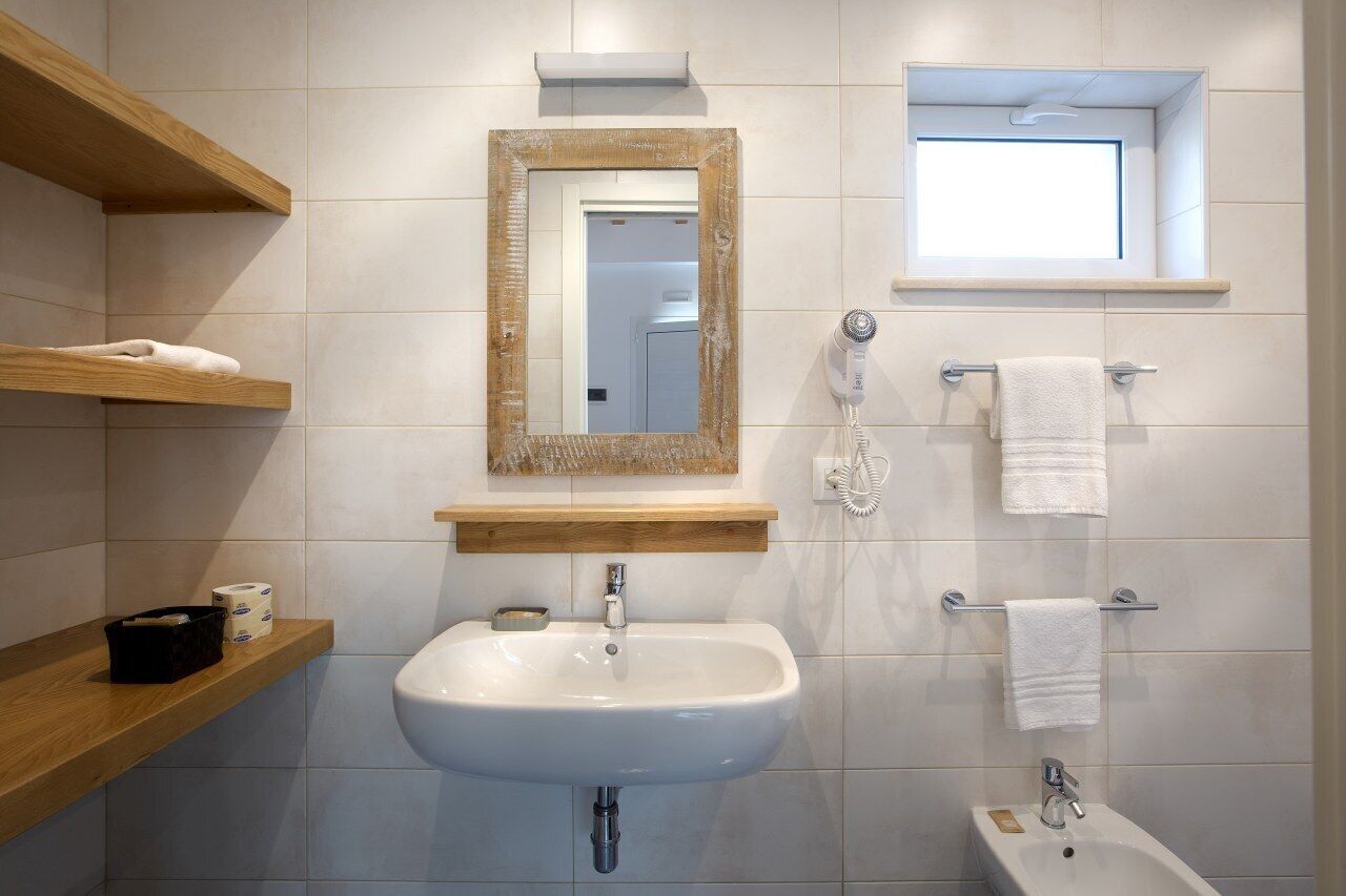 A bathroom with a white sink, wooden shelves, a mirror, a towel rack, and a window.