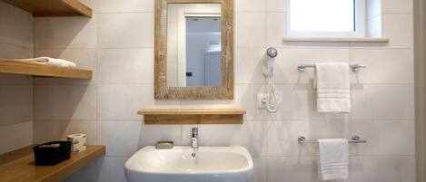 A bathroom with a white sink, wooden shelves, a mirror, a towel rack, and a window.